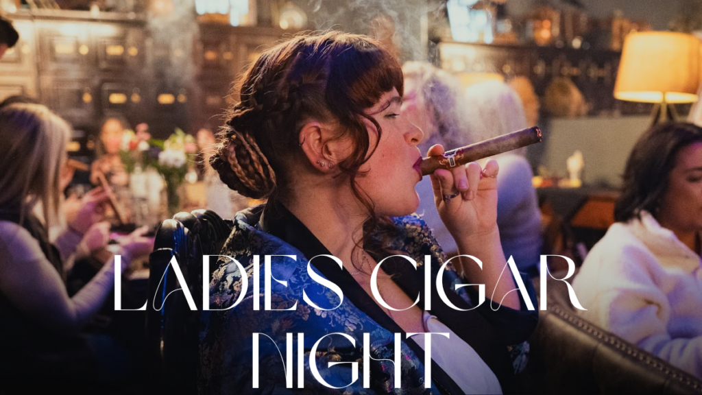 Woman with braided hair wearing a blue smoking jacket enjoying a cigar inside Mayor’s Cigar Lounge at Vineyard Market.
